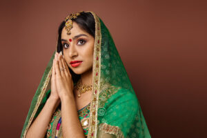 pretty indian woman in traditional costume with bindi dot showing praying gesture and looking away